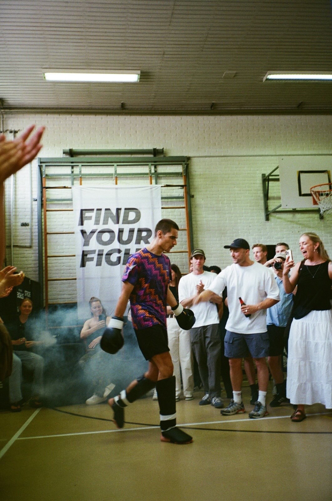 A boxer in colorful gear walks past a cheering crowd in a gym. A "FIND YOUR FIGHT" banner hangs in the background.