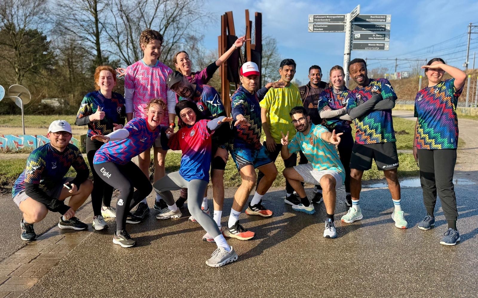 A diverse group of people in colorful athletic gear poses energetically outdoors; signs and trees are visible in the background.