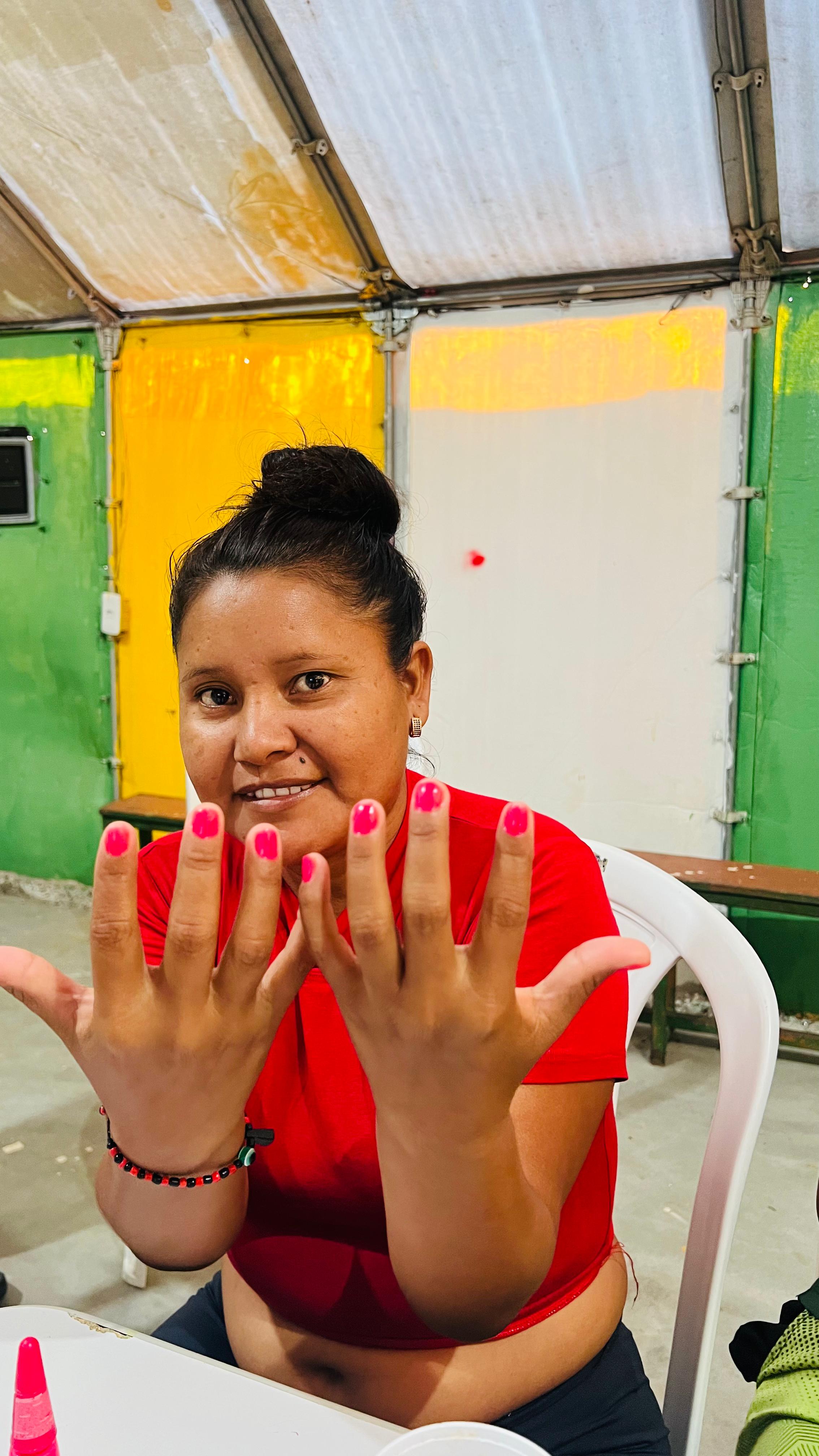 Woman in a red shirt shows off her bright pink manicured nails in a room with green and yellow walls