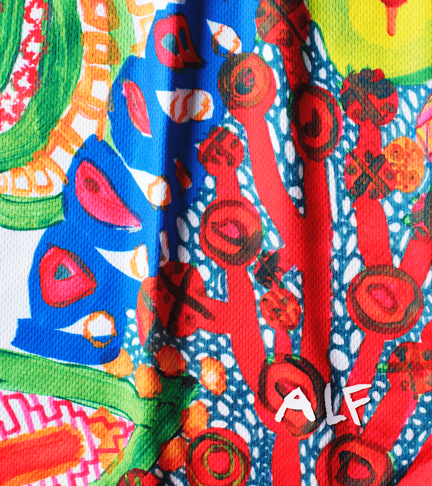 A vibrant, abstract T-shirt featuring a mix of colorful patterns, shapes, and symbols, with prominent reds, blues, yellows, and greens. Refugee sports sportswear impact