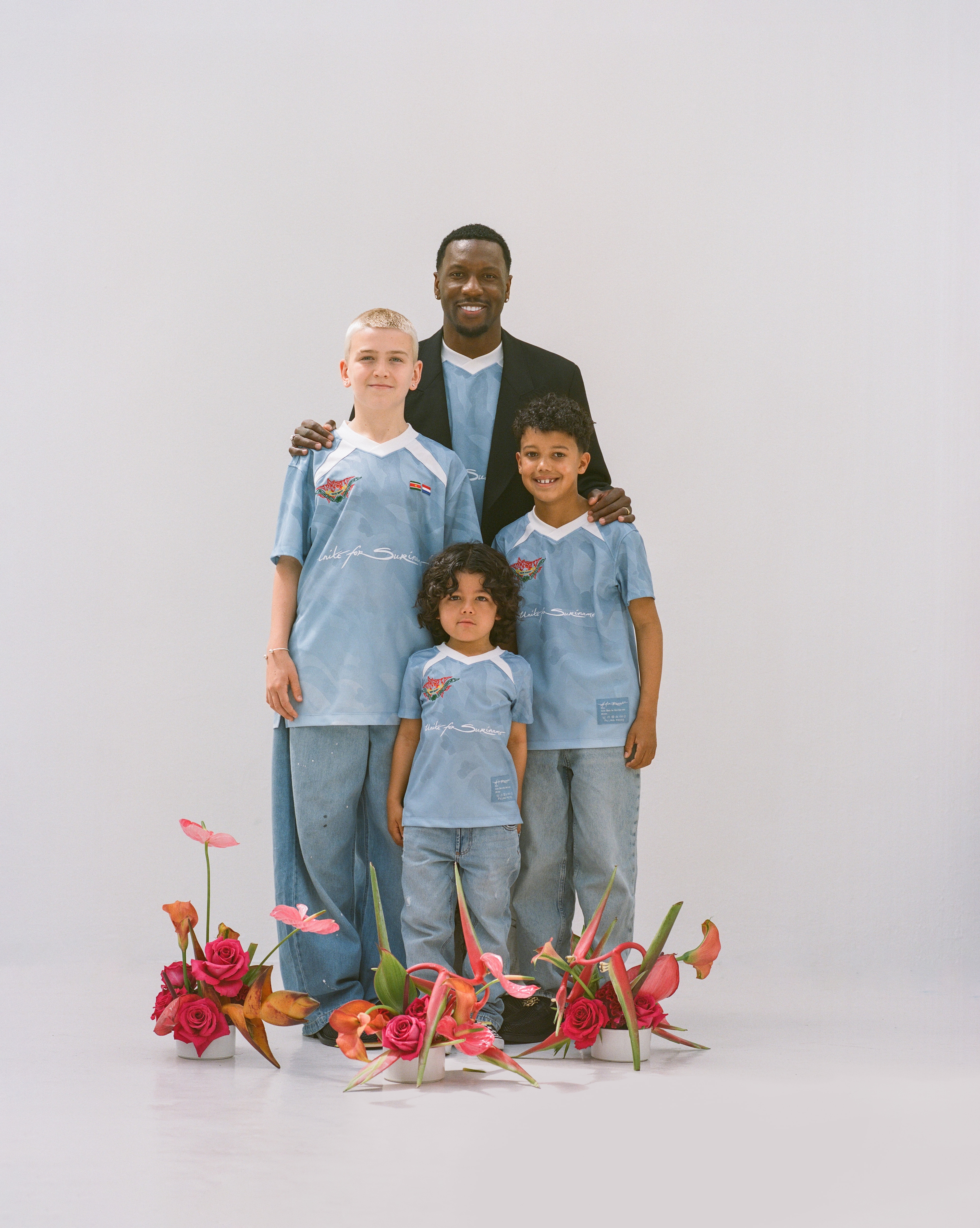 A father and 3 sons from Surinamese decent wearing limited edition shirts for Keti Koti 2026 posing with flowers surrounding them